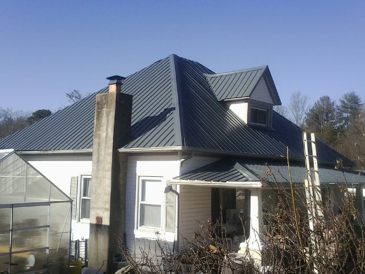 Dark blue standing seam metal roof on a white farmhouse with dormer — Slate & Tile Roof Repair by Roofing Brothers in Fairview