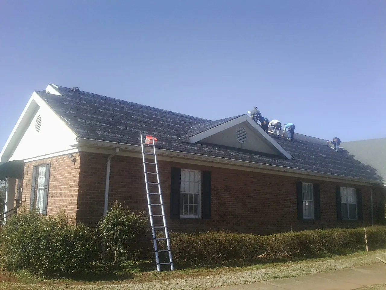 Crew tearing shingles off a brick ranch roof with a ladder set — Emergency Roof Repair work by our crew in Fairview
